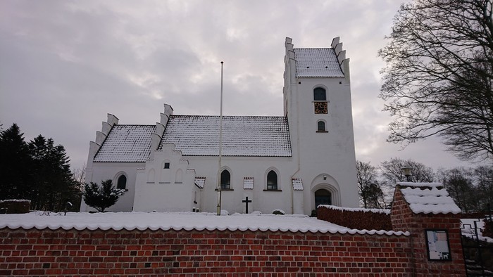 En snedækket hvid kirke med tårn og mur.