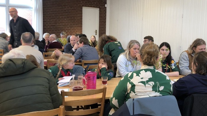 Gruppe af mennesker samlet indendørs til et fælles måltid eller arrangement med afslappet påklædning og festlige borddekorationer.