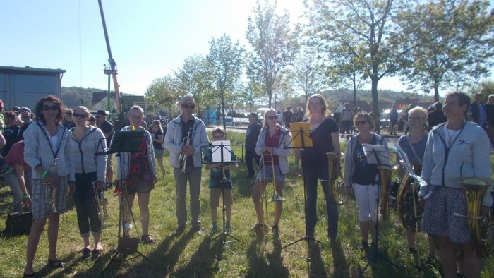 Eine Gruppe von Menschen steht im Freien und singt in Notenheften.