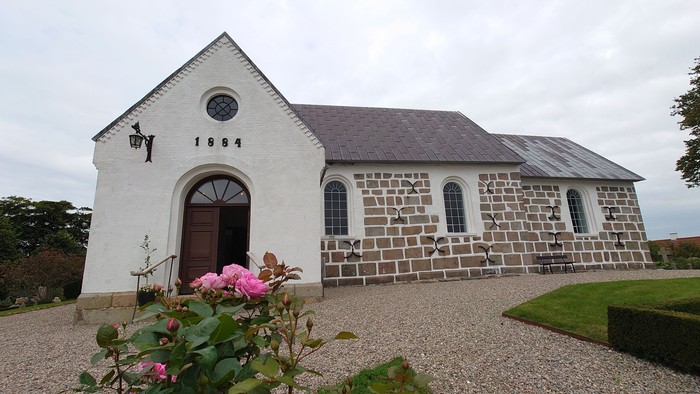 En lille, hvidkalket kapel med mursten og rosbuske foran