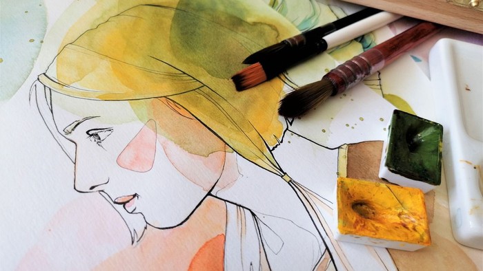 Ein Aquarellbild, das das Profil einer Frau zeigt, ist von Pinseln, Aquarellfarben und Malutensilien auf einem Tisch umgeben.