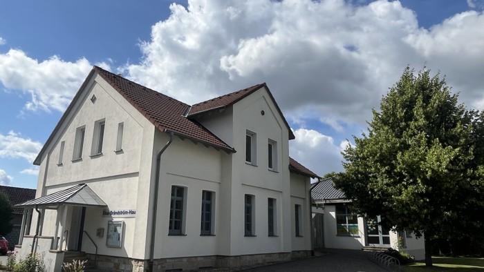 Das Bild zeigt das Laggenbecker Gemeindehaus, ein weiß verputztes Gebäude mit einem Anbau rechts.