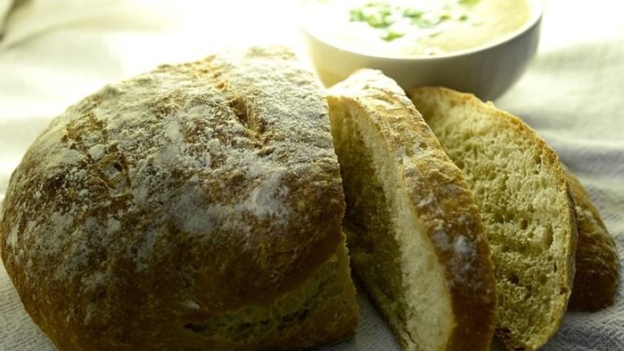 A loaf of bread with several slices cut, next to a bowl of soup.