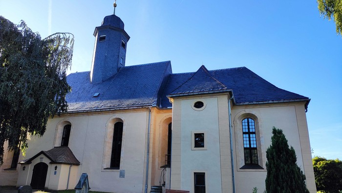 Weiße Kirche mit hohem Turm und blauen Dach unter klarem Himmel