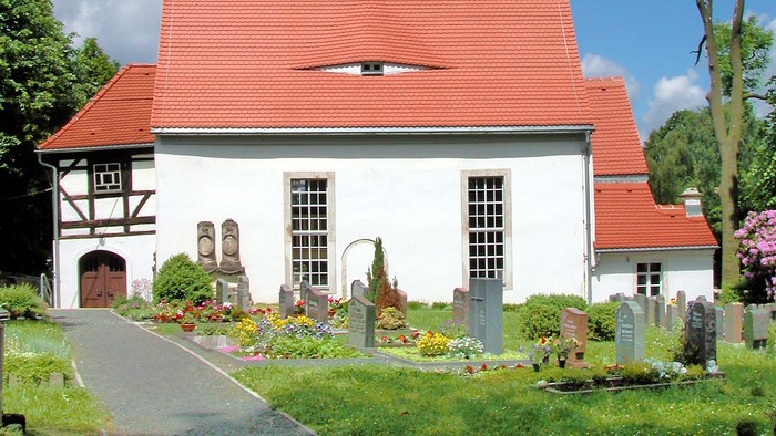 Kleine weiße Kirche mit rotem Dach und schwarzem Turm.
