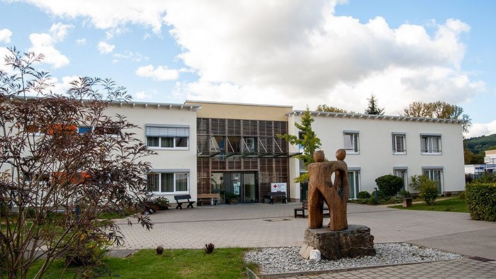 Modernes Gebäude mit Skulptur im Vordergrund, gepflegtem Garten und klarem Himmel