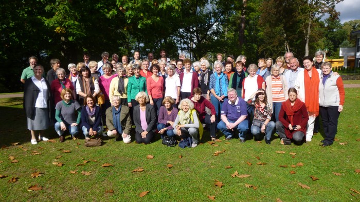 Gruppe von Menschen, die im Freien auf einer grasbewachsenen Fläche mit Bäumen posieren.