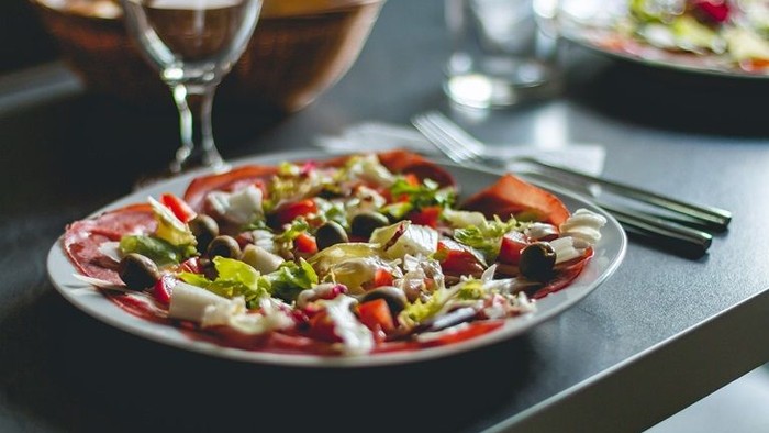 Ein Pizzateller mit verschiedenen Belägen steht auf einem Tisch mit Besteck und Getränken.