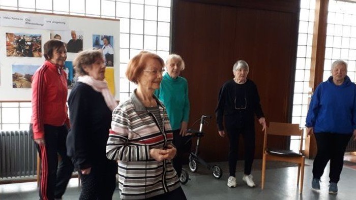 Eine Gruppe von Menschen in einem Raum, einige betrachten Fotos an der Wand.