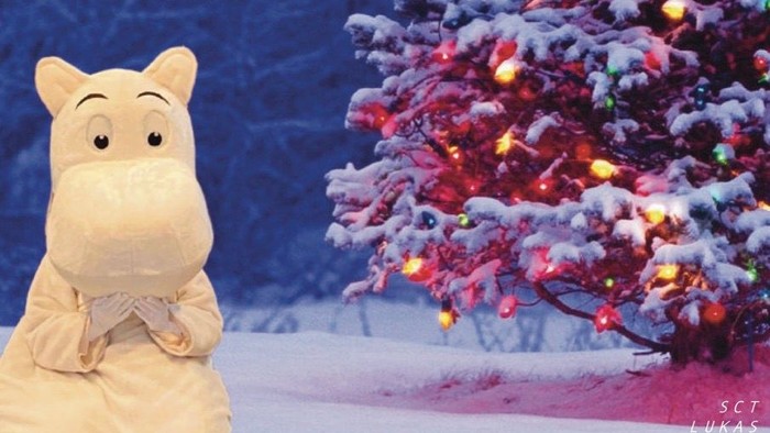 En kæledyrdukke står foran en juletree med lys.