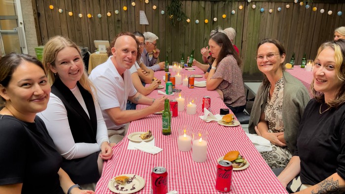 En gruppe af venner sidder sammen ved en festligt dækket bord med mad og drikkevarer i en trægart.
