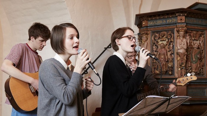 Drei Musiker proben in einer Kirche mit einem alten Kruzifix.