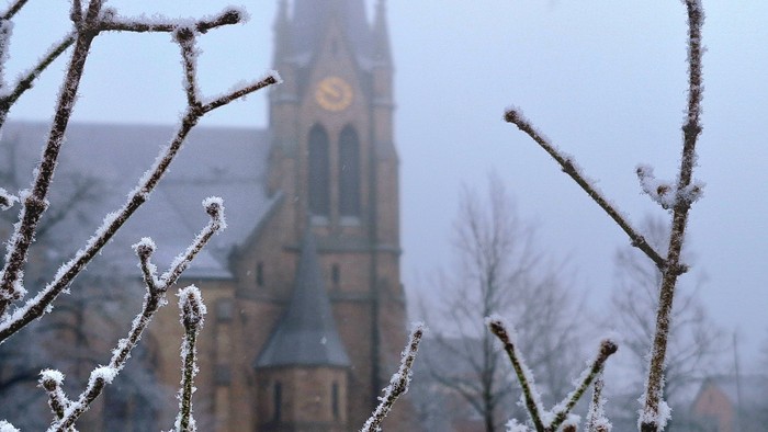 Schneebedeckte Äste im Vordergrund, Kirche mit Uhrturm im Hintergrund.