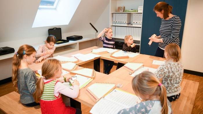 Ein Klassenzimmer, in dem Kinder an einer Aktivität teilnehmen, während eine Lehrkraft sie an einem großen Tisch anleitet.