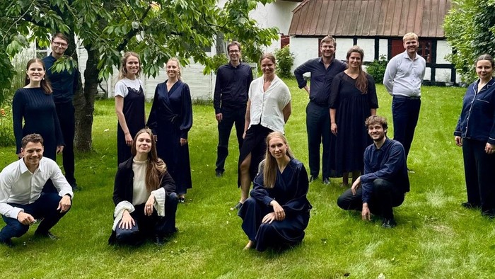 Gruppe af mennesker i koordineret mørkt tøj, der poser udendørs i en haveindstilling.