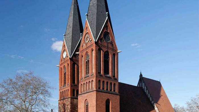 Große rote Backsteinkirche mit zwei hohen Türmen und spitzen Dächern vor blauem Himmel