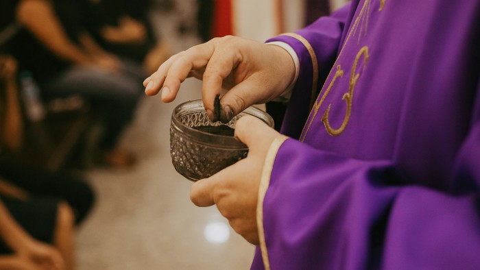 Eine Person in violettem Gewand, die einen kleinen Kommunionskelch hält und während einer religiösen Zeremonie Wein austeilt.