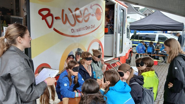 Gruppe von Kindern und Erwachsenen versammelt sich um eine mobile Wahlkabine für eine Veranstaltung mit dem Namen „B-Wee“.