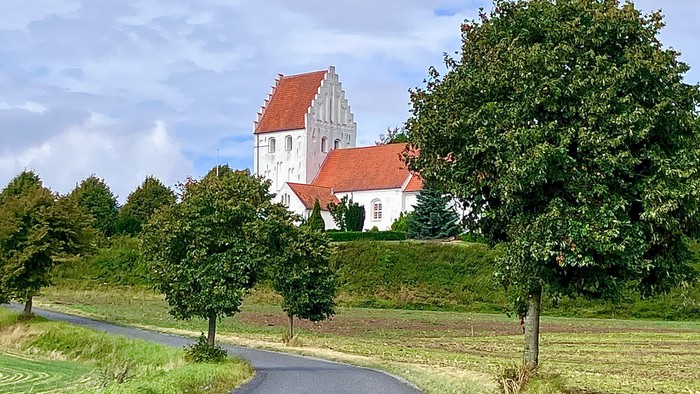 Malerværdig landevej, der fører til en charmerende hvid kirke med rødt tag.