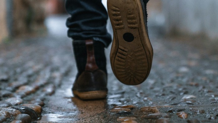 Man ser en mands støvler på en våd gade. Han går.