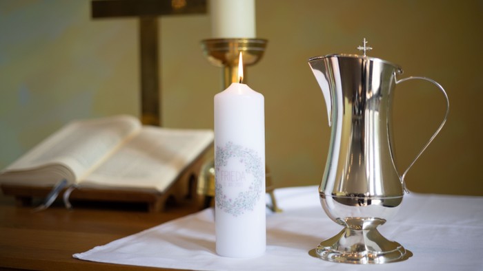 Heiliger Altaraufbau mit einer geöffneten Bibel, einer brennenden Kerze und einem silbernen Weihwassergefäß.