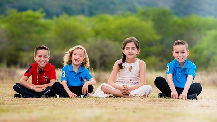 Vier fröhliche Kinder, die glücklich zusammen auf einer üppigen, grünen Wiese im Freien sitzen.