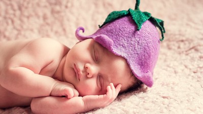 Ein schlafendes Baby mit einer lila Strumpfhut-Mütze mit grünen Blättern.