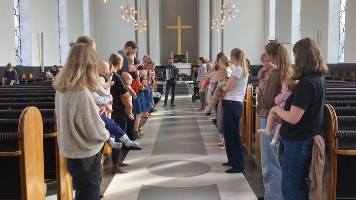 Babyer og forældre synger og danser i Skt. Lukas Kirke til babykravlekoncert med harmonikaspiller Jesper Vinther