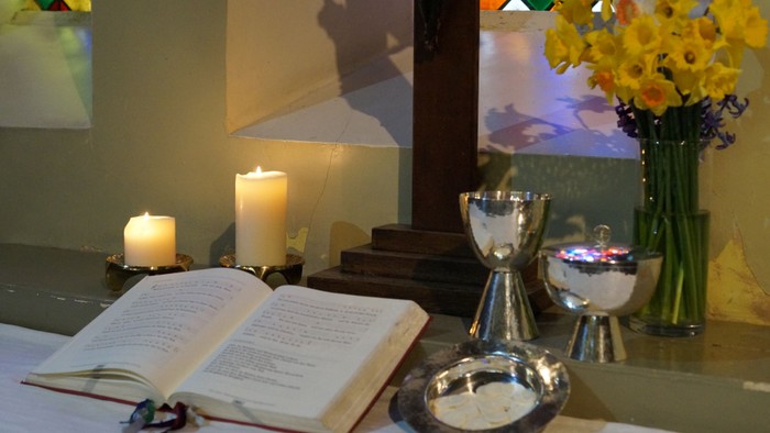 Ein Altar mit brennenden Kerzen, einem Buch, Kelchen und einer Vase mit gelben Blumen
