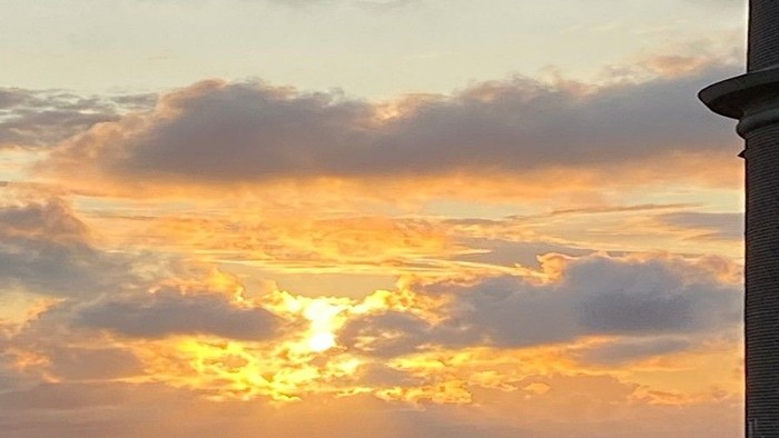 En rødgul solgang med skyer og en del af et hus på højre side