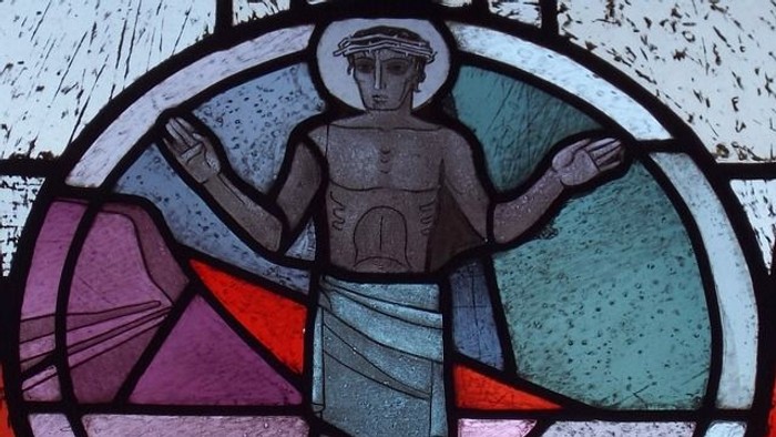 Das Bild zeigt ein buntes Kirchenfenster mit einer religiösen Figur.