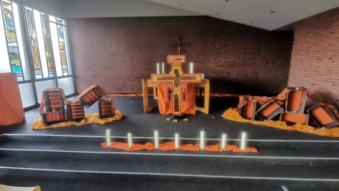 Ein Kircheninnenraum mit orangefarbenen Altarschmuckelementen und verstreuten Requisiten, wahrscheinlich für eine thematische Veranstaltung oder einen Gottesdienst.
