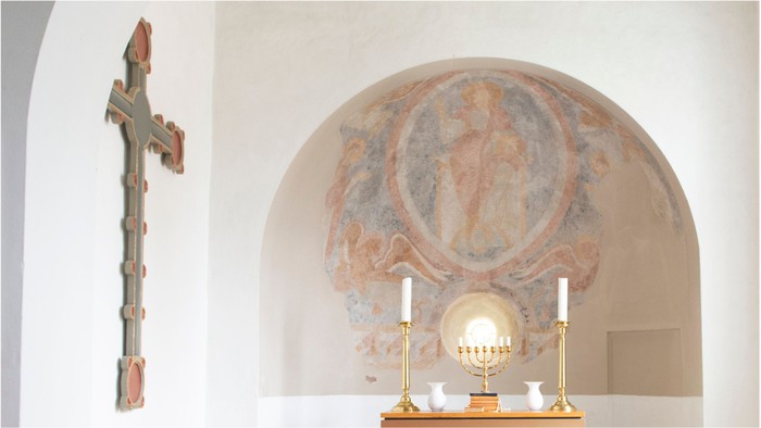 Elegant kapelkrog med et krucifiks, prægtig vægfresko og gyldent kandelaber med lys.