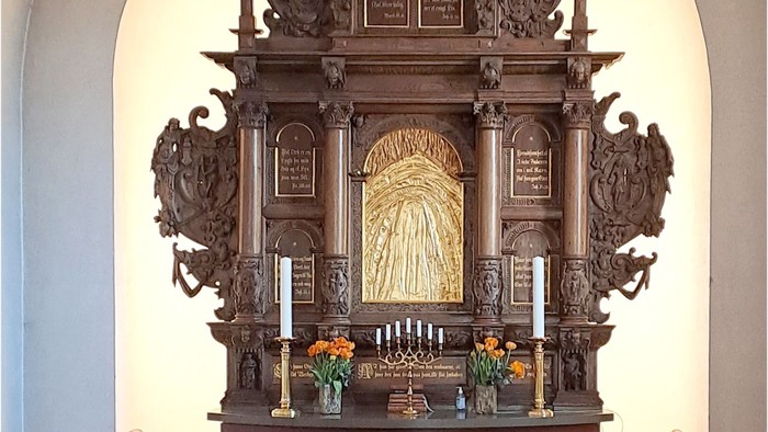 Indviklet træalter med religiøse udskæringer, lys, blomster og indskrevne plaketter.