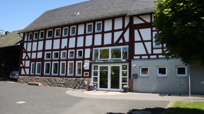 Das Bild zeigt ein traditionelles Fachwerkhaus mit einem großen Fenster und einem gepflasterten Vorplatz.