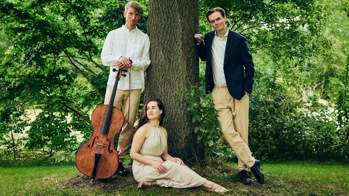 Musikere poser udendørs med en cello, elegant klædt i en rolig haveomgivelse.