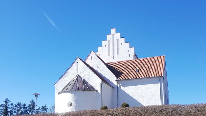 En charmerende hvid kirke med et stejlt, trappetaget mod en klar blå himmel.