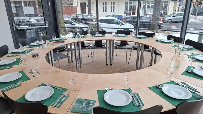 Elegante runde Esstafel-Einrichtung mit grünen Tischläufern, Tellern und Weingläsern in einer modernen Indoor-Location.