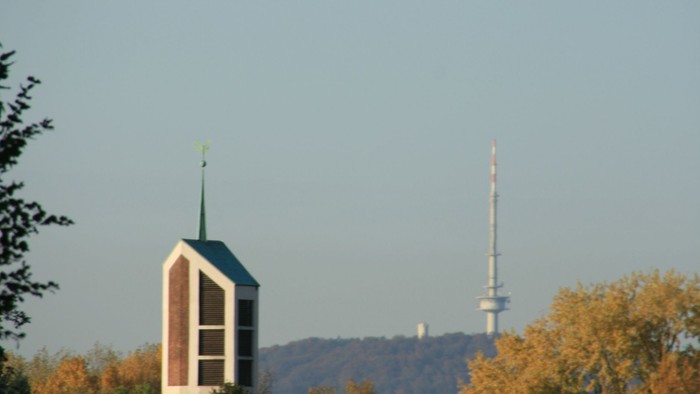 Städtische Skyline mit Kirchturm, Wohnhaustdächern und einem hohen Sendemast vor herbstlichem Laub.