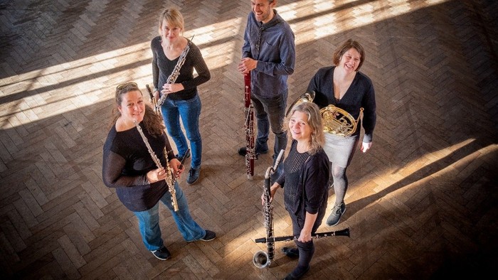 Fem musikere poser med instrumenter i et rum med trægulve.
