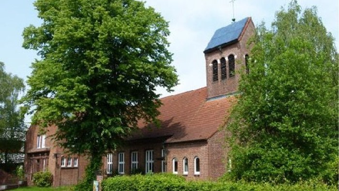 Eine malerische Backsteinkirche mit einem hohen Glockenturm, umgeben von üppigem Grün und Bäumen.