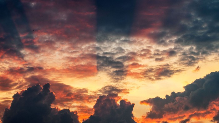 Lebhafter Sonnenuntergang mit dramatischen Wolken in Orange-, Rot- und Grautönen.