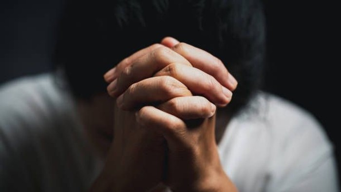 Person with hands clasped together, appearing in contemplation or prayer.