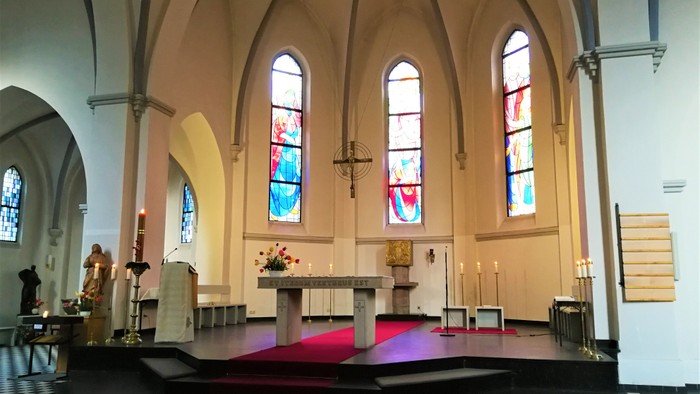 Innenraum einer Kirche mit Altarraum, farbigen Glasfenstern und Holzbänken