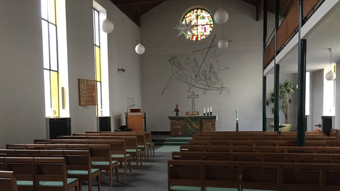 Leere Kirche mit Holzbänken und großem Kirchenfenster