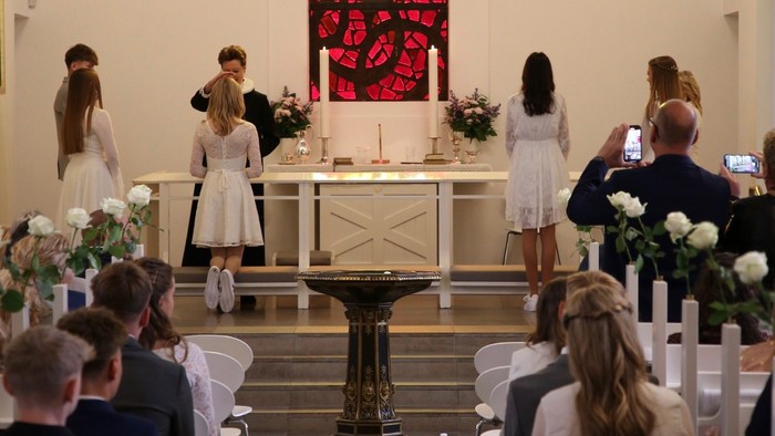 En bryllupsceremoni finder sted i en kirke med gæster, brudefoljet og præst ved alteret.