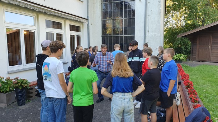Gruppe von Menschen, die vor einem Haus steht, einige sitzen auf einer Bank und unterhalten sich.