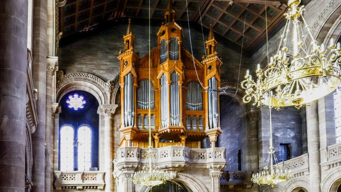 Orgue en bois doré suspendu dans une église avec vitraux et lustres.