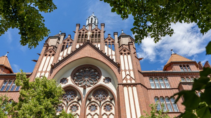 Gothische Architektur mit großen Fensterbogen und Türmen, umgeben von Bäumen