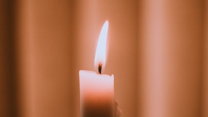 Eine brennende Kerze vor einem beigen Vorhang.